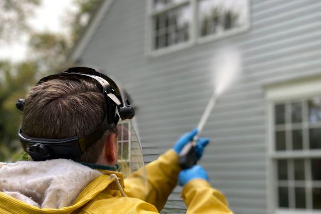 Worker in protective gear pressure washing house siding